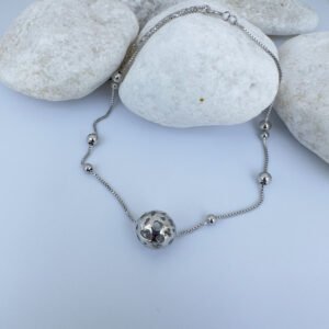 Silver anklet with a sphere charm and smaller balls around the chain draped over white rocks.
