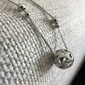 Silver anklet with a globe like ball as the main feature and two pairs of smaller balls one bigger than the other on a grey background.