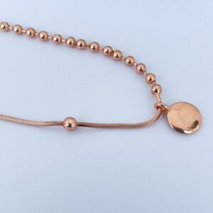 Close up of a rose gold anklet with a round charm and lots of small balls.