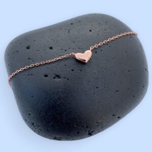 Stunning rose gold anklet with a cute solid rose gold heart charm, on a black rock.
