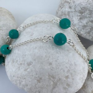 Silver anklet with four turquoise balls evenly spaced around the ankle bracelet, on a white rock.