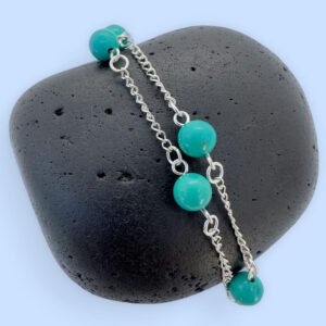 Silver anklet with four turquoise balls evenly spaced around the ankle bracelet, presented on a black rock.