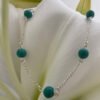 A shiny silver anklet with turquiose balls around the chain, in a beach chic style