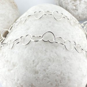 Identical interlinking dainty silver hearts ankle bracelet on a white rock.