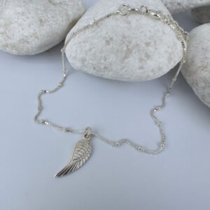 Silver anklet with a single angel wing pendant on white rocks.
