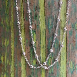 Silver ankle bracelet with small silver balls around the chain at equal distance, on a wooden background with green painted stripes.