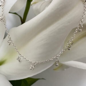 A gracious looking anklet with lots of small sterling silver balls hanging from it, equally spaced all the way around a dainty ankle chain, presented on a white lily petal.