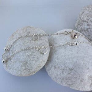 Beautiful silver anklet with hoop and ball charms equally spaced around on a white rock.