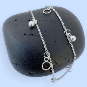 Beautiful silver anklet with hoop and ball charms equally spaced around, on a black rock.