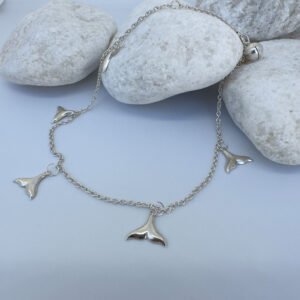 Anklet in silver with whale tail charms equally spaced around presented on white rocks.
