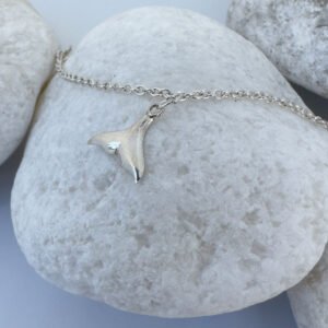 Anklet in silver with whale tail charms equally spaced around presented on a white rock.
