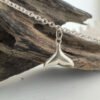 End of a whale's tail sterling silver charm on an ankle chain hung from some driftwood.