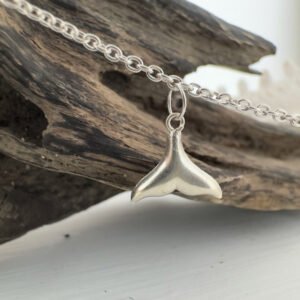 End of a whale's tail sterling silver charm on an ankle chain hung from some driftwood.