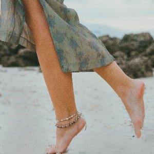 Legs of a lady walking in the beach wearing petite anklets.